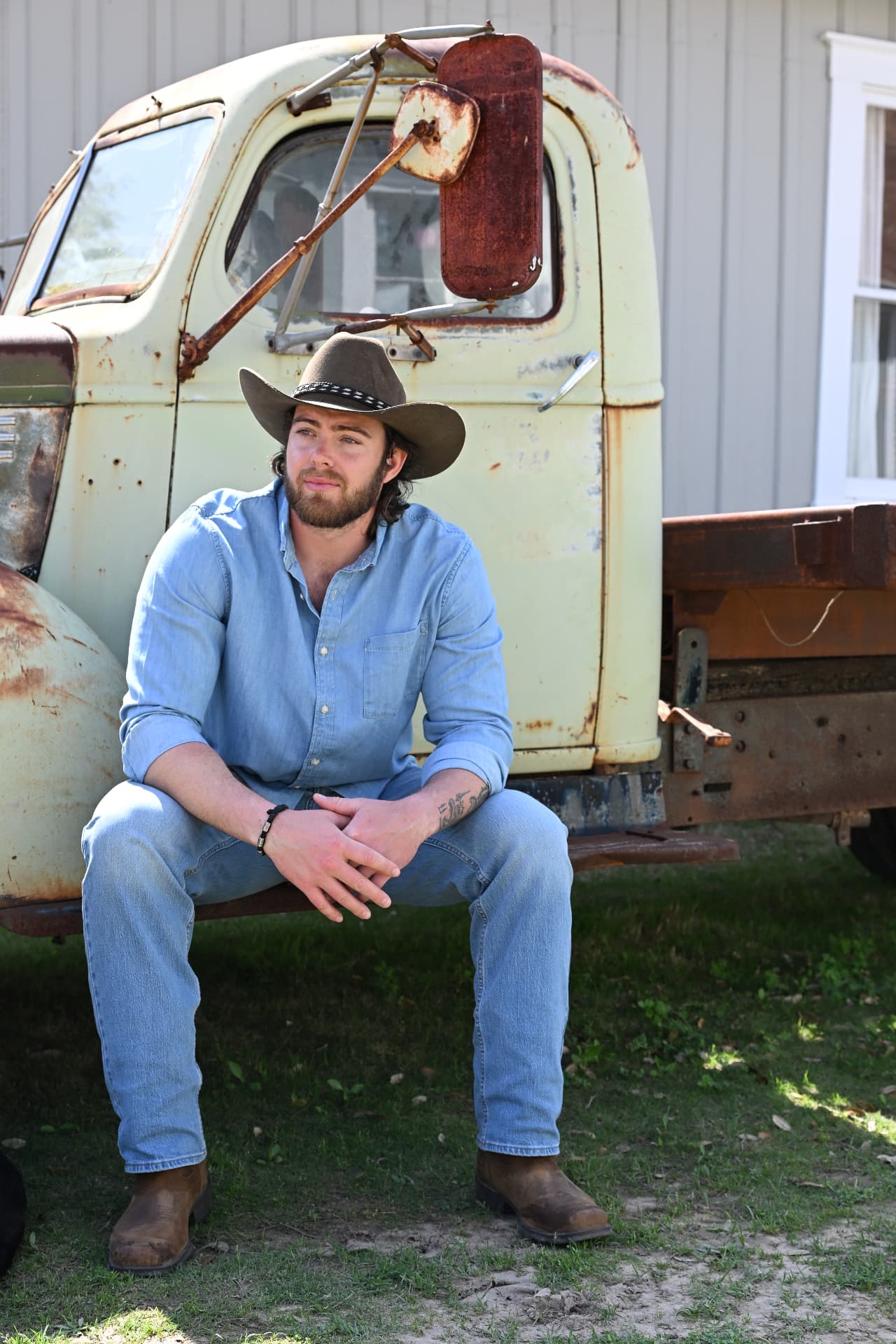 Jake Colletti seated on the tailgate of a vintage pickup truck in denim and a cowboy hat